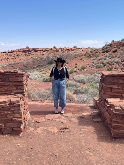 Woman standing inside circular stone ruins with desert landscape visible behind