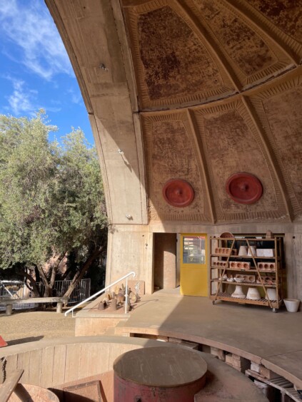 Curved concrete workspace with pottery wheels and ceramic pieces on shelves